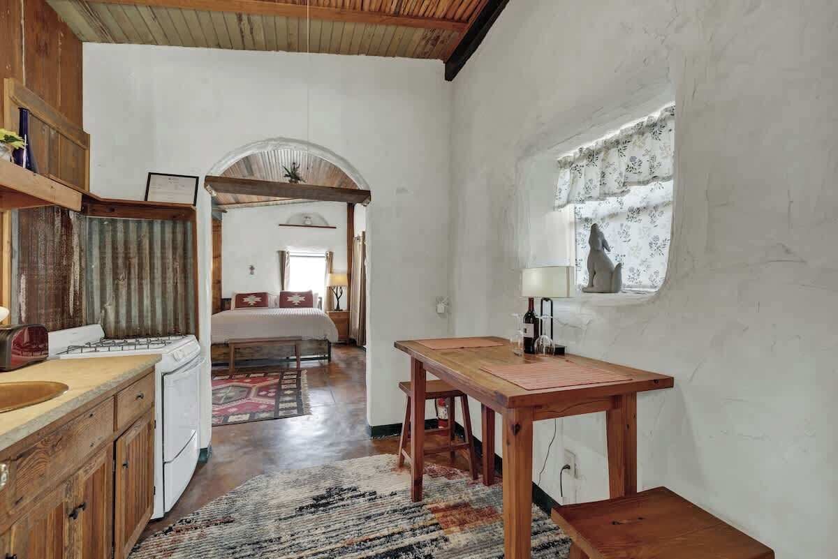 A compact kitchen with wooden cabinets, a dining table, and a window with a curtain.
