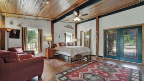 A spacious bedroom with a large bed, a wooden ceiling, and a view through a glass door. - Sonora Casita Hot-tub Four Minutes to Marktplatz! (Fredericksburg)
