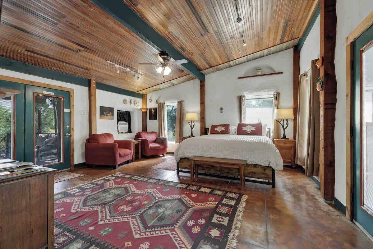 A spacious bedroom with a large bed, a wooden ceiling, and a patterned rug.