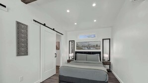 A bedroom with a bed, a nightstand, a wall-mounted artwork, and a door. - Evergreen Escape W/hot-tub 5 Min to Downtown! (Fredericksburg)