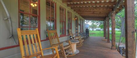 A covered outdoor seating area with wooden chairs and tables, wooden beams overhead, and large windows with red trim.