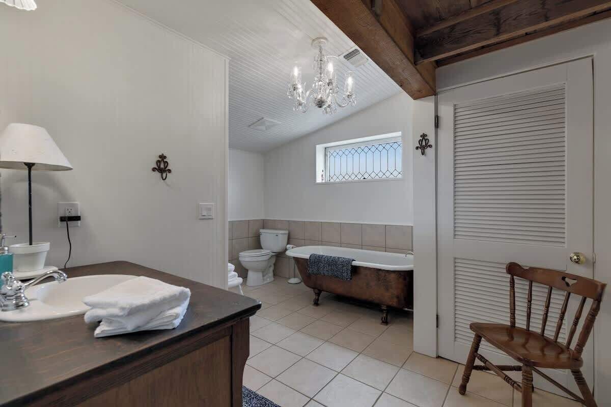 A bathroom with a wooden vanity, a freestanding bathtub, a chandelier, and a window with bars.