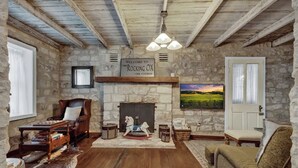 A rustic room with a stone wall, wooden floor, a fireplace, a rocking horse, and a painting of a landscape. - Rocking Ox Gasthaus and Barn Cabin (Fredericksburg)
