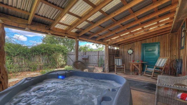 Ein Whirlpool unter einer Holzpergola mit einem rustikalen Holzzaun und einer grünen Tür im Hintergrund.