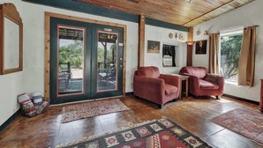 Ein Zimmer mit Holzboden, einer großen Tür mit Glasscheiben, zwei Ledersofas, einem kleinen Tisch und einem gemusterten Teppich.