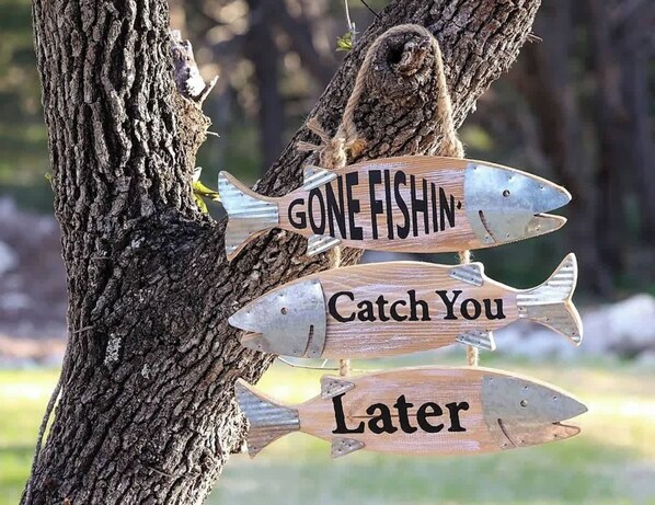 A wooden sign with fish shapes and text saying "GONE FISHIN' Catch You Later" hanging on a tree. - Serene Guadalupe River Getaway-river Access! (Spring Branch)