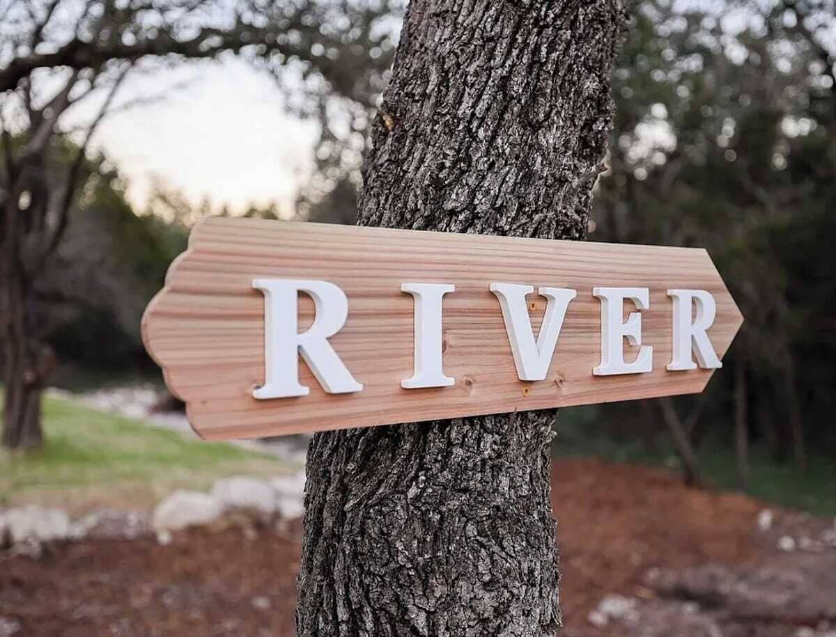 A wooden sign with the word "RIVER" mounted on a tree.