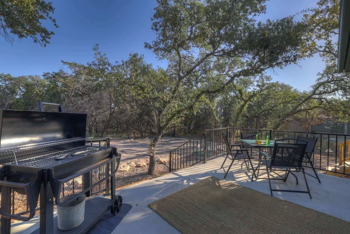 Une terrasse extérieure avec un barbecue, un espace salon et une vue sur les arbres.
