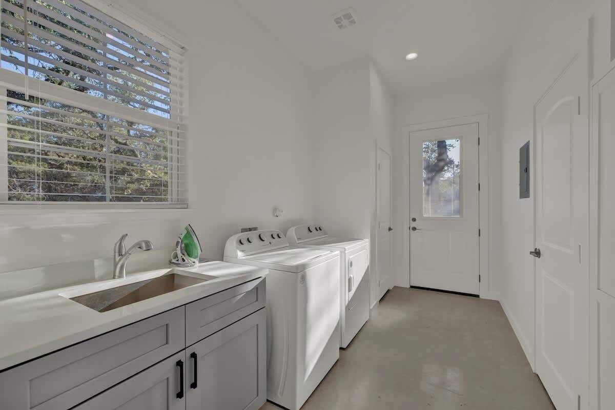 A modern laundry room with a sink, two washing machines, and a dryer.