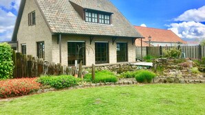 Une maison traditionnelle avec un toit en pente, des murs en pierre et un jardin bien entretenu, agrémenté de diverses plantes et fleurs.