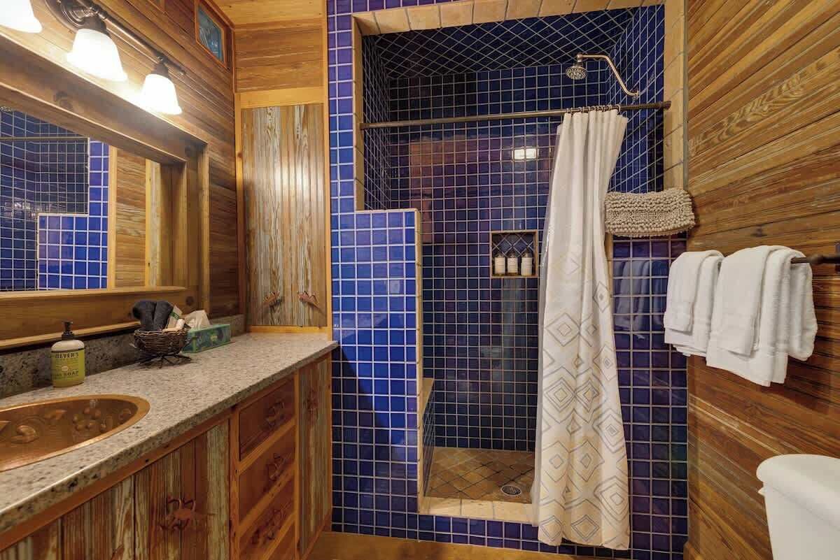 A bathroom with a wooden vanity, a blue-tiled shower area, and a hanging shower curtain.