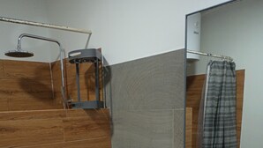 Et moderne badeværelse med bruseafsnit i træ, et hvidt toilet, en vask med spejl over og en lille potteplante på vasken.