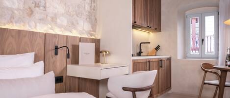 Une chambre d’hôtel moderne avec un mur en pierre, des meubles en bois, un lit blanc et une petite kitchenette.