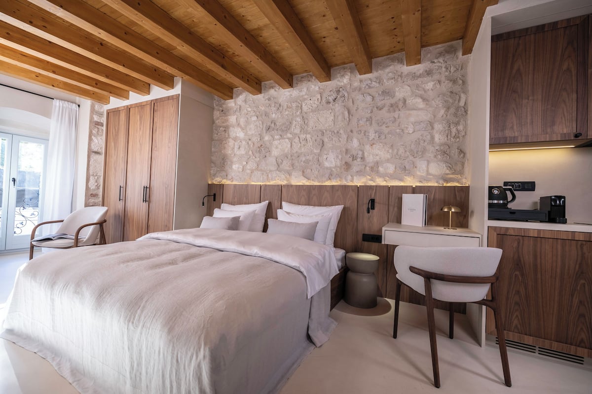 Un dormitorio moderno con una cama grande, cabecera de madera, pared de piedra y una pequeña cocina.