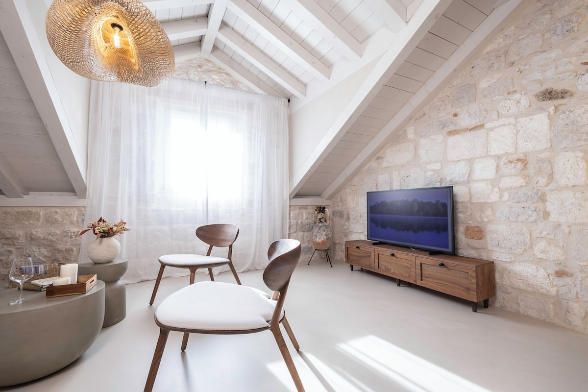 Un loft moderno con paredes de piedra a la vista, un televisor grande y una zona de estar acogedora con una mesa de centro redonda y sillones.