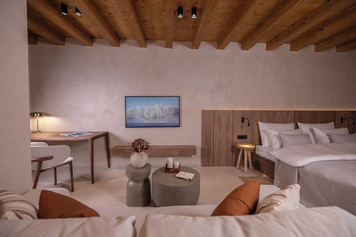 Un dormitorio moderno con techo de madera, una cama con ropa de cama blanca, un escritorio con silla y una pequeña mesa redonda con adornos.