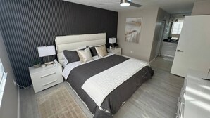 Ein modernes Schlafzimmer mit einem großen Bett, Nachttischen, einem Deckenventilator und Blick in die angrenzende Küche.