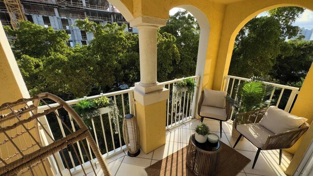 Ein Balkon mit einem Korbstuhl, einem kleinen Tisch mit einer Pflanze und Blick auf ein Bauprojekt.