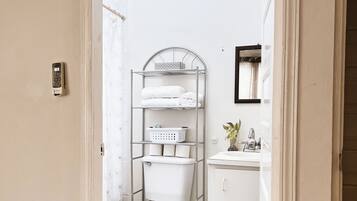 Une salle de bain comprenant des toilettes, une étagère en métal avec des serviettes, un panier et un petit coin lavabo.