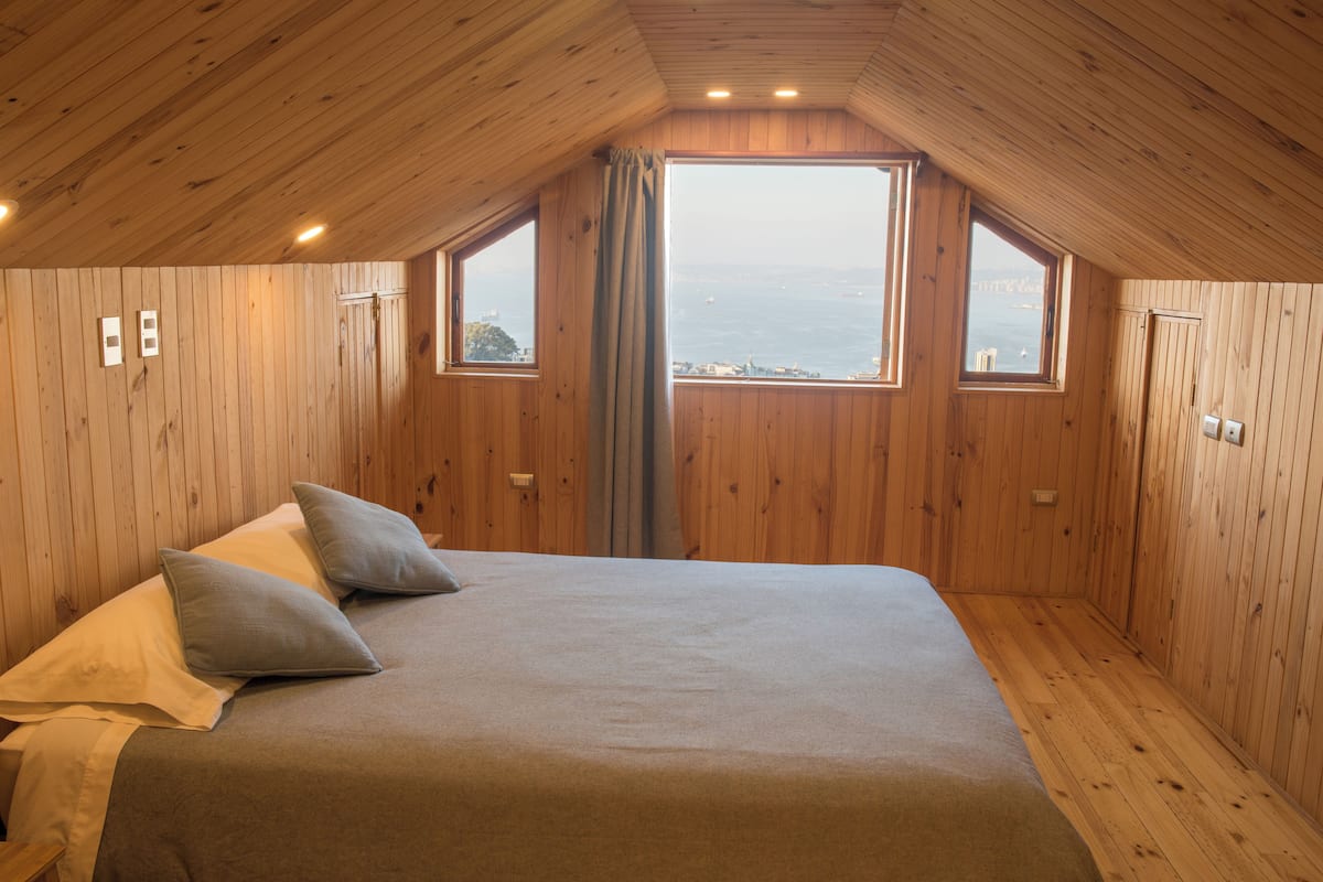 A wooden-paneled bedroom with a large bed, two windows, and a view of the sea.