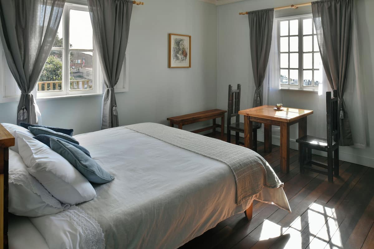 A room with a bed, a wooden table, a chair, and a window with curtains.