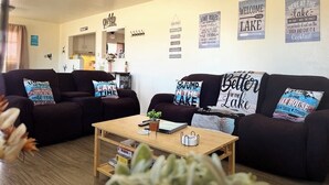 A cozy living room with two dark sofas, a wooden coffee table, and various lake-themed wall decorations.
