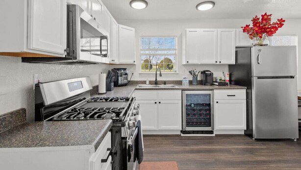 A modern kitchen with white cabinets, stainless steel appliances, and a built-in wine cooler. - All American Cottage (Wichita Falls)