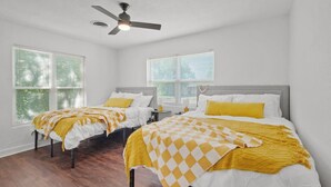 A bedroom with two beds, white walls, wooden flooring, and a ceiling fan. - All American Lone Star (Wichita Falls)