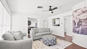 A modern living room with a grey sofa, a patterned ottoman, and a ceiling fan. - All American Lone Star (Wichita Falls)