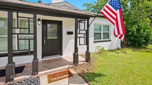 A house with a black door, a welcome mat, and an American flag. - All American Lone Star (Wichita Falls)