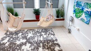A room with two macramé hammocks, a patterned rug, potted plants, and a wall-mounted air conditioner. - Charming 3-bedroom house in delightful Isabela with Wi-Fi, AC

 (Isabela)