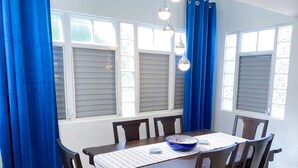 A dining area with a table, chairs, blue curtains, and windows with blinds. - Charming 3-bedroom house in delightful Isabela with Wi-Fi, AC

 (Isabela)