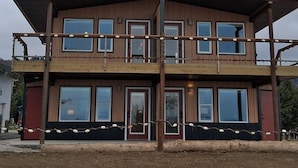 A two-story building with a flat roof, large windows, and a balcony with string lights. - GLACIER SUITE, BEACH WALK INN, UPPER LEVEL UNIT
FEATURING HOMER'S FANTASTIC VIEW (Homer)