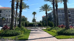 A pathway lined with palm trees, leading to a building with a fountain in the center. - 4-bedroom apartment in enchanting Orlando with WiFi, AC (Orlando)