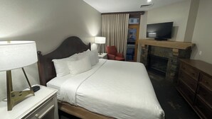 Habitación de hotel con una cama grande, televisión, chimenea, escritorio con lámpara y una silla.