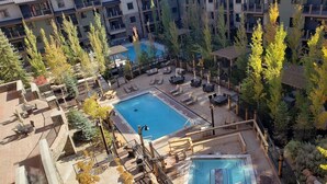 Un área de piscina en la azotea con sillones de descanso y una piscina pequeña, rodeada de árboles y un edificio de varios pisos.