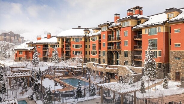Un hotel de varios pisos con zona de piscina, mobiliario exterior y paisajes nevados.
