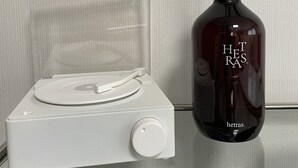 Un reproductor de música blanco con una cubierta plástica transparente y una botella oscura con pajitas negras y el texto