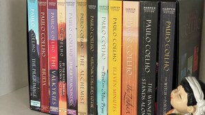 Una estantería con una colección de libros de Paulo Coelho, incluyendo títulos como "El Alquimista" y "La esposa del Alquimista".