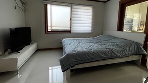 Un dormitorio con cama, televisor sobre un mueble, ventana con persianas y espejo con marco decorativo.