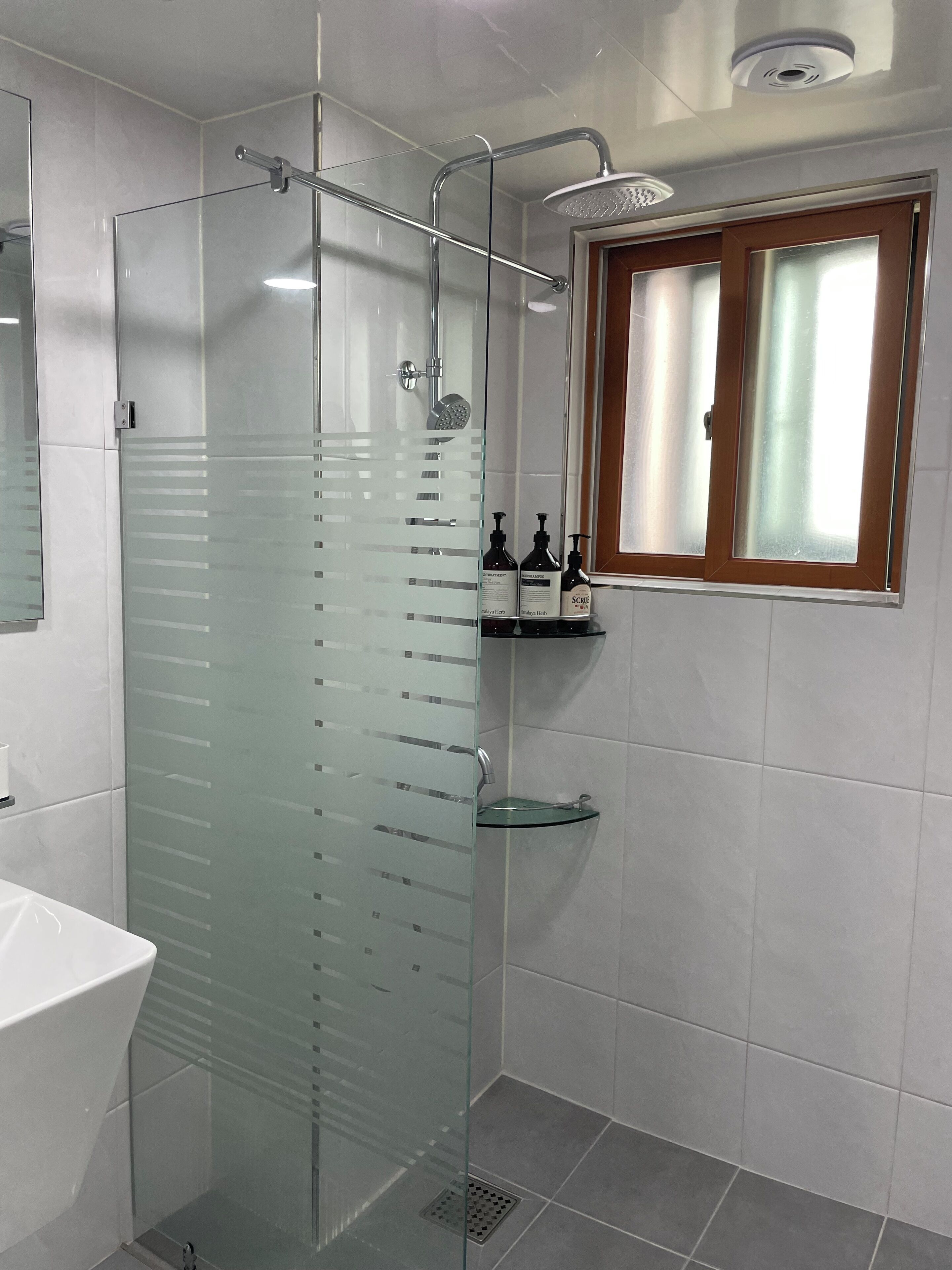 A modern bathroom with a glass-enclosed shower, a white sink, and a window with frosted glass.