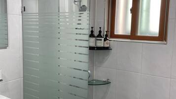 A modern bathroom with a glass-enclosed shower, a white sink, and a window with frosted glass.