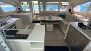 A compact galley with a stove, sink, and storage cabinets. There is a small seating area with a table and cushions. - Eleuthera Sailing Catamaran Adventure (Freetown)