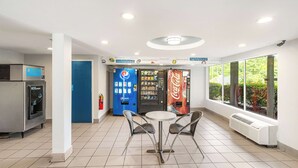 A clean, well-lit indoor area with vending machines, a Coca-Cola fridge, and a table with chairs. - Studio 6 Augusta, Ga (Augusta)
