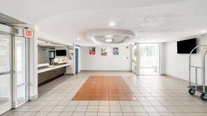 A spacious lobby with a tiled floor, an exit sign, a reception desk, a cart, and a television on the wall. - Studio 6 Augusta, Ga (Augusta)