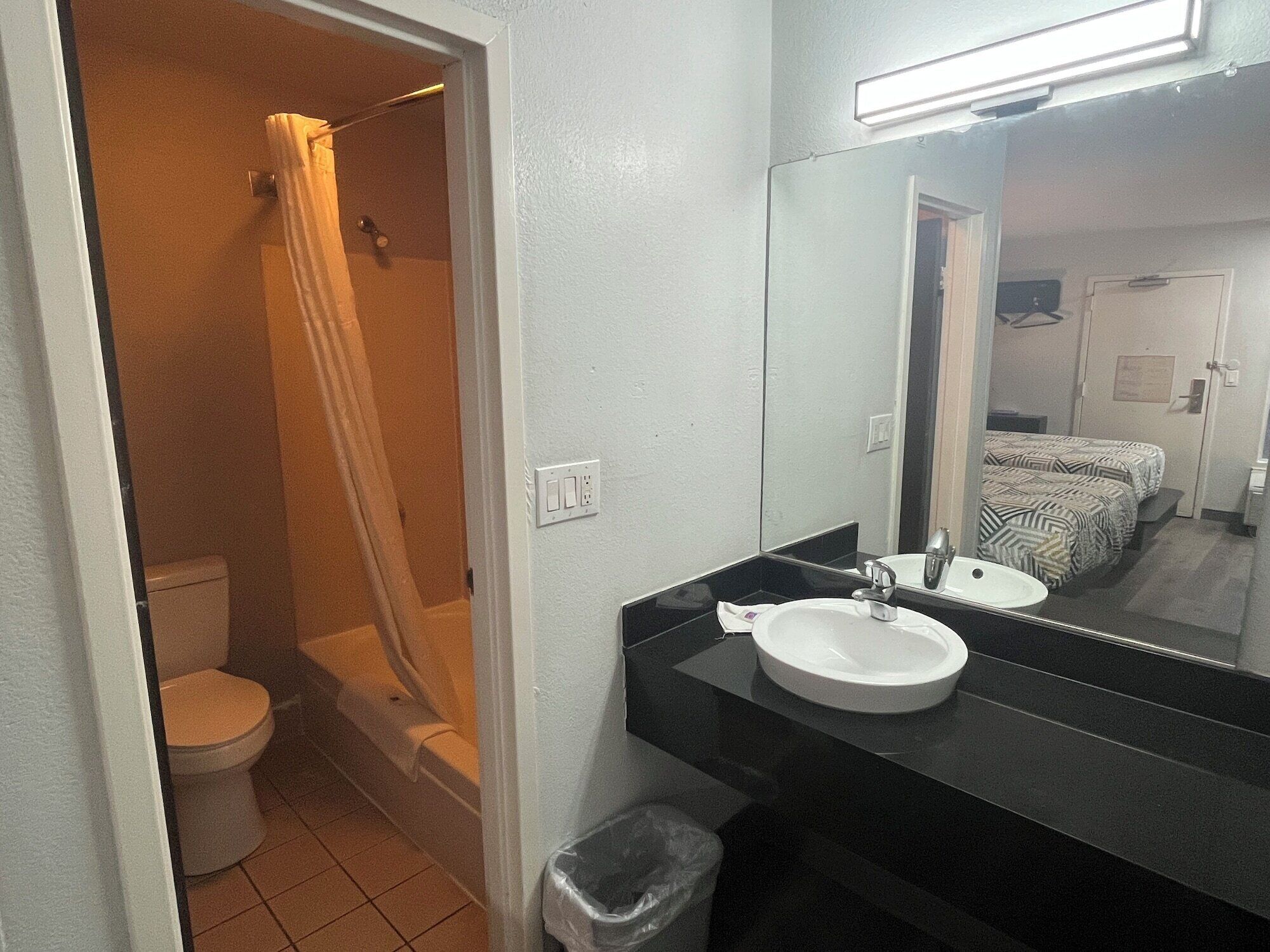 A bathroom with a toilet, shower, sink, and a mirror.