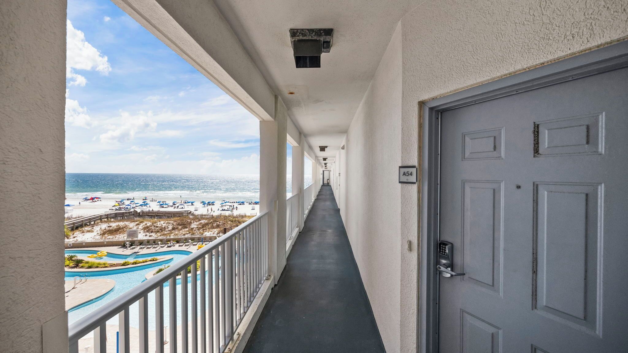 Un pasillo con vista a una playa y una piscina, que conduce a una puerta con la etiqueta A54.