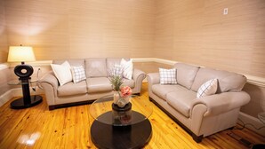 Un salon avec deux canapés beige, une table basse en verre agrémentée d’objets décoratifs, un lampadaire et un plancher en bois.