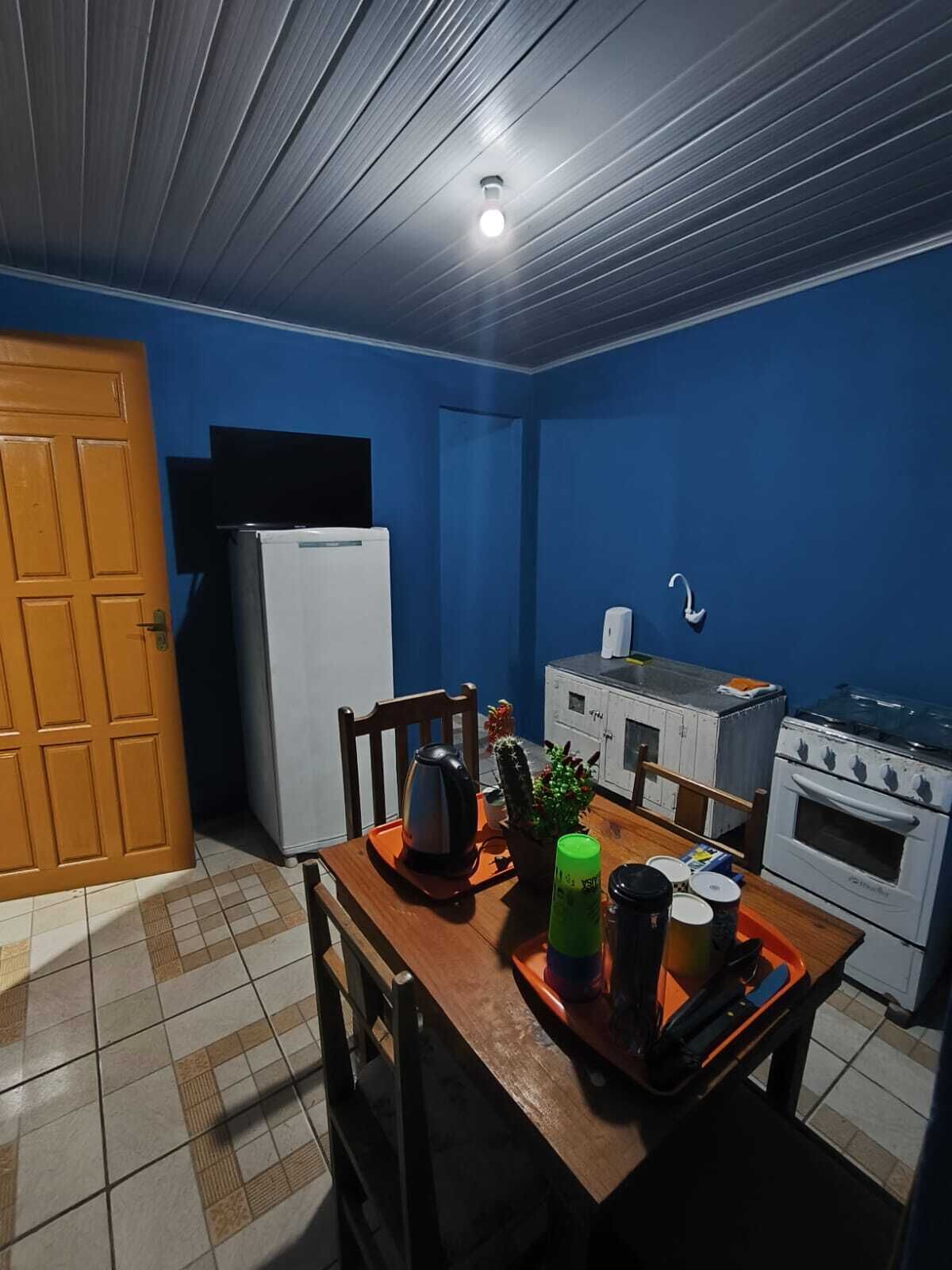 Une cuisine de taille réduite avec des murs bleus, une table à manger en bois, un réfrigérateur, une cuisinière et un évier.