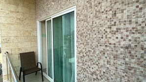 Un balcone con una sedia, una porta vetrata e un muro piastrellato.